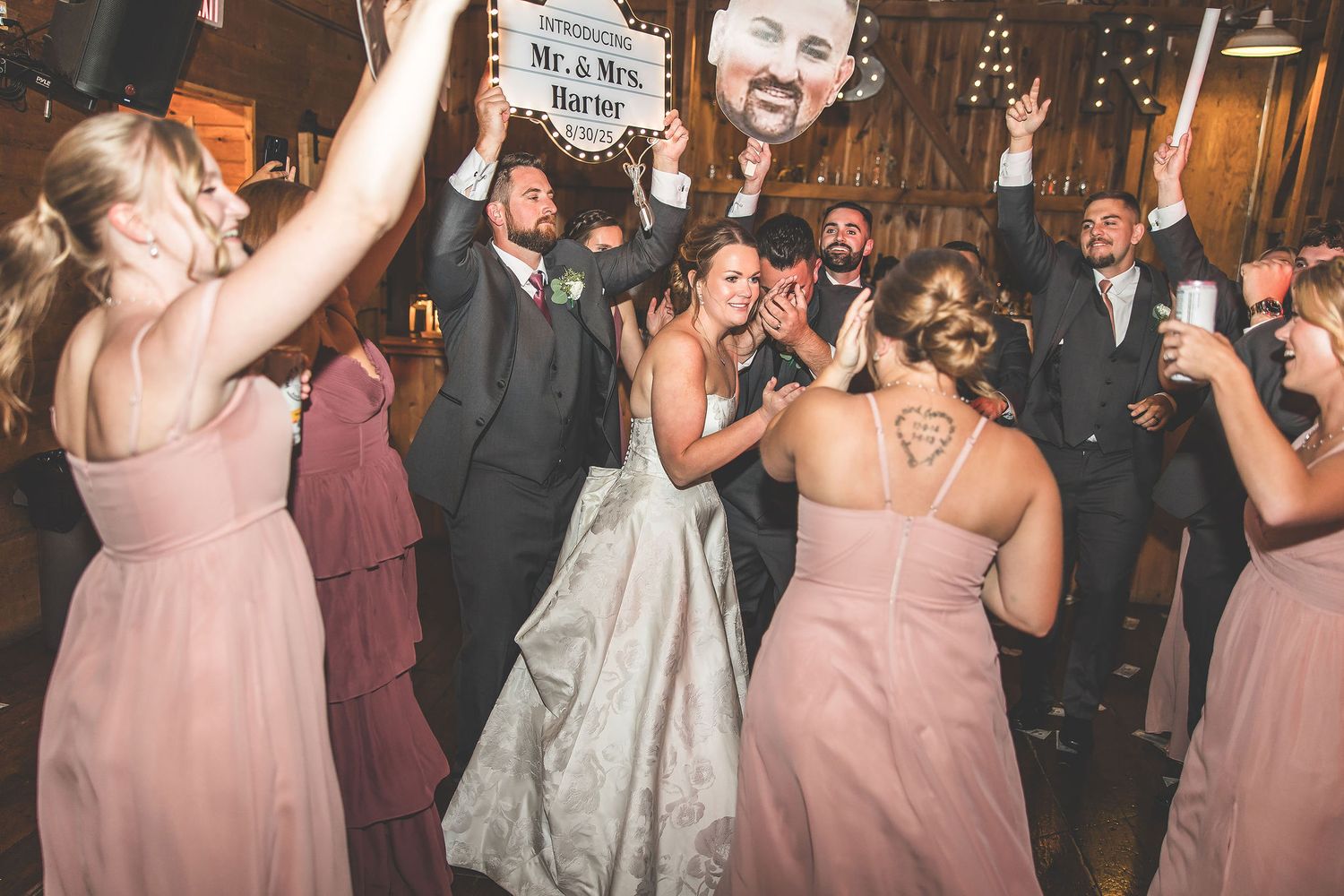 Wedding guests dancing and celebrating on wooden dance floor with string lights overhead.