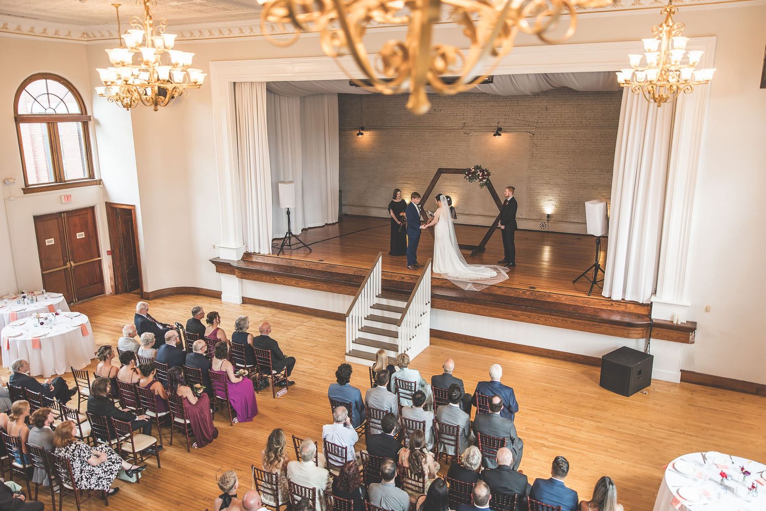 Wedding venue with natural light streaming through arched windows and elegant chandelier fixtures.