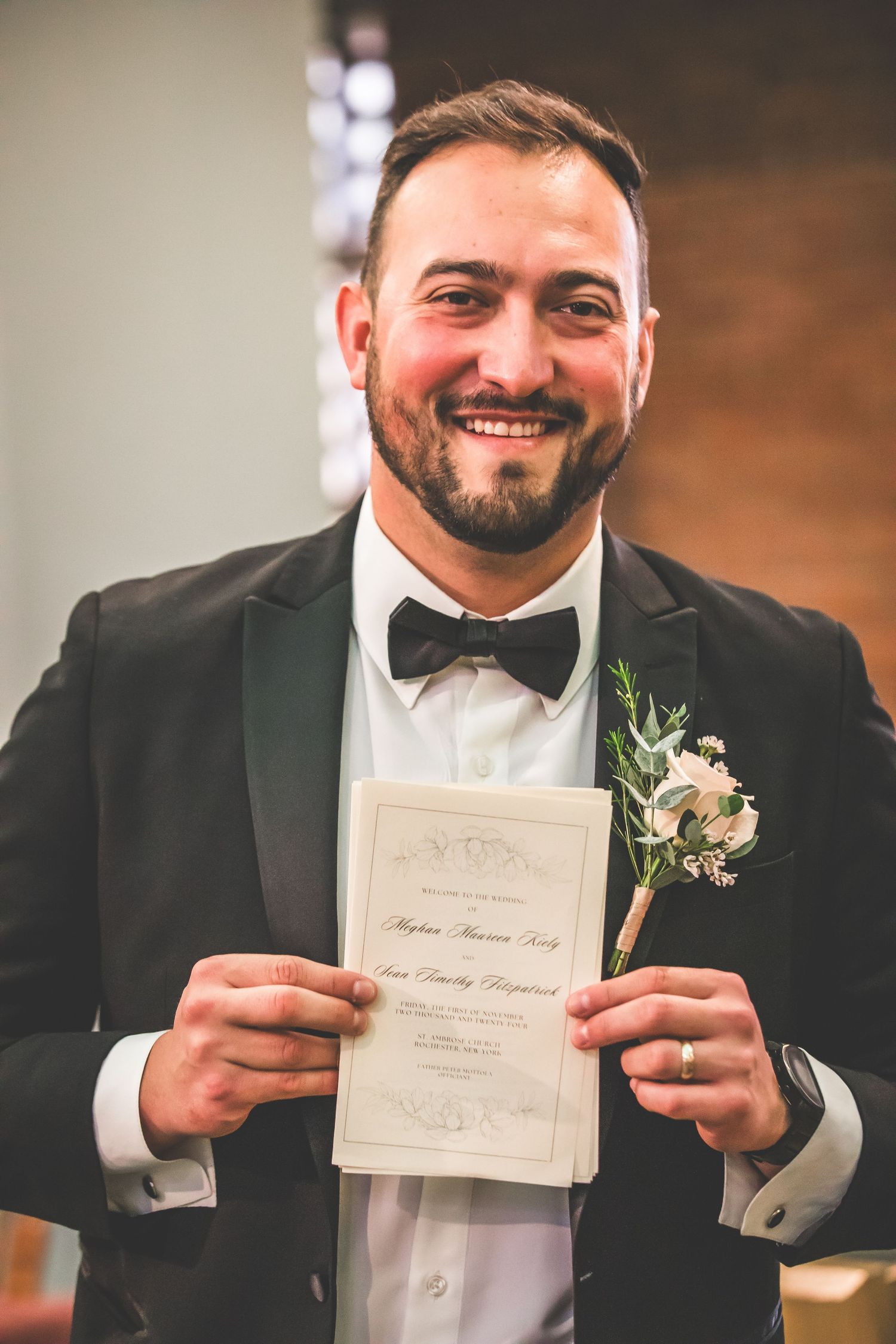Wedding photo of a groom in black tuxedo holding up a marriage certificate with boutonniere.