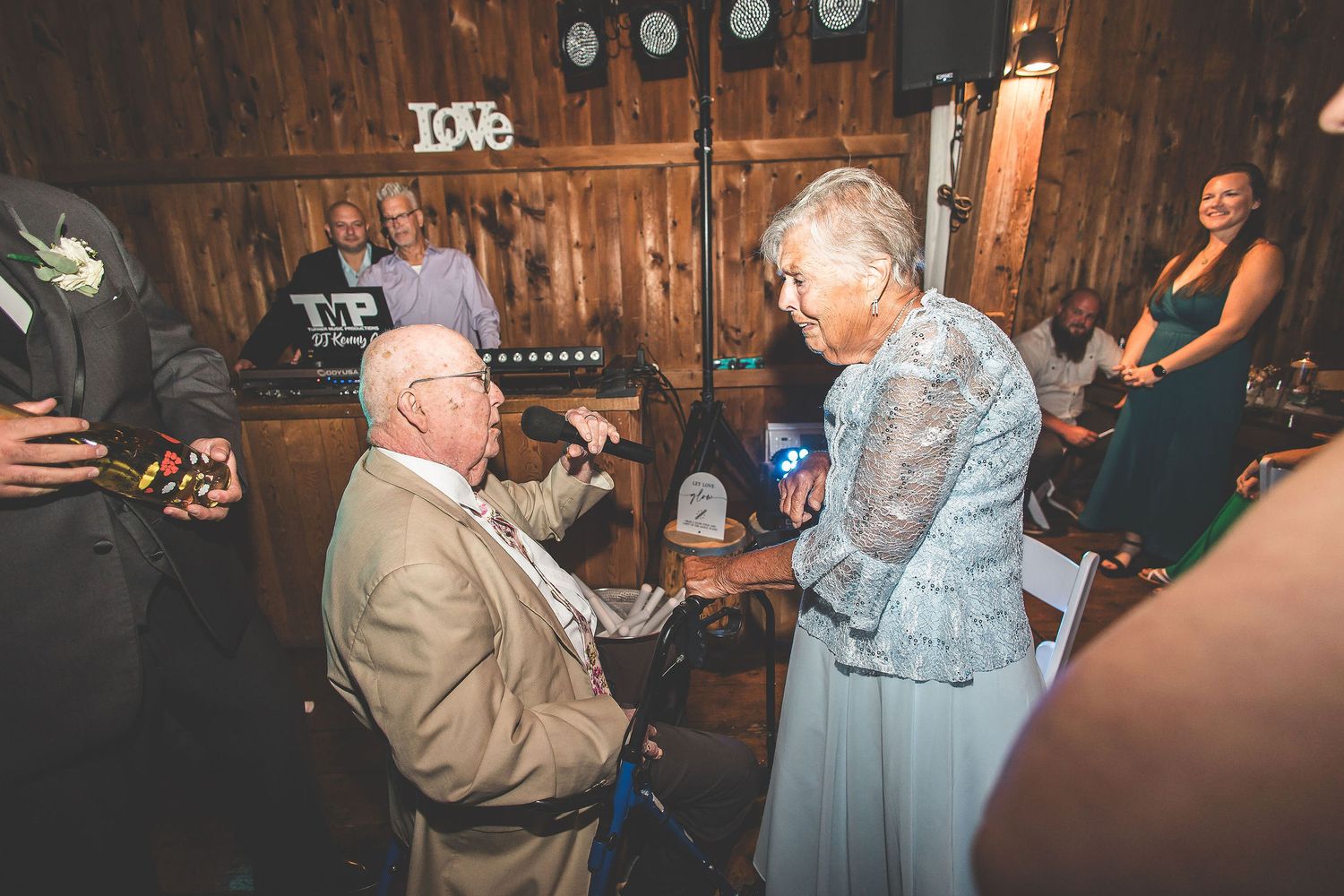 Wedding reception guests dance and celebrate on a rustic wooden barn dance floor with string lights overhead.