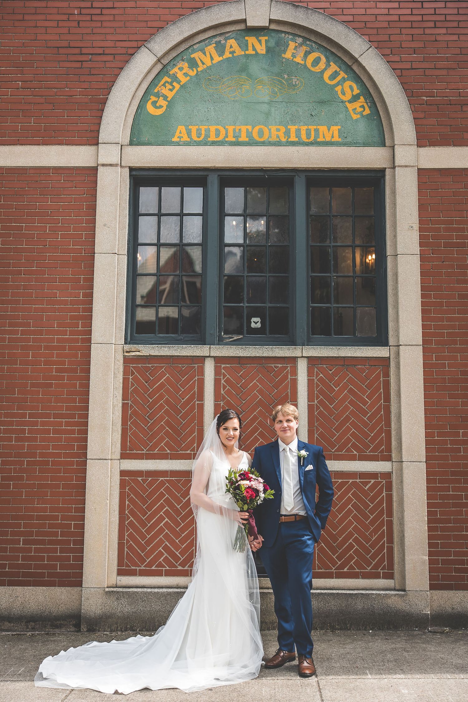 Wedding couple poses in front of historic German House Auditorium brick building entrance.