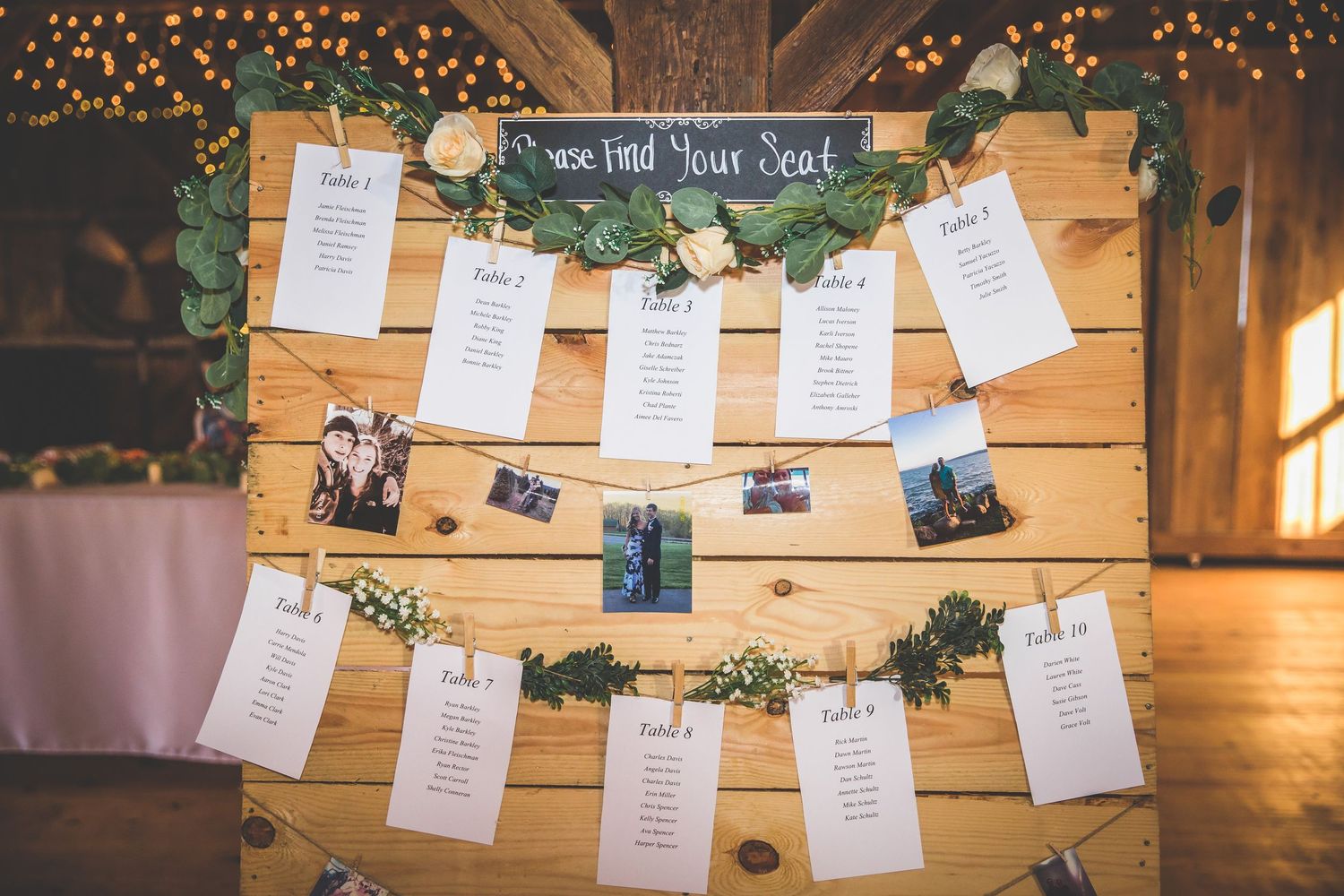 Wedding seating chart display with photos and cards strung on twine with fairy lights.