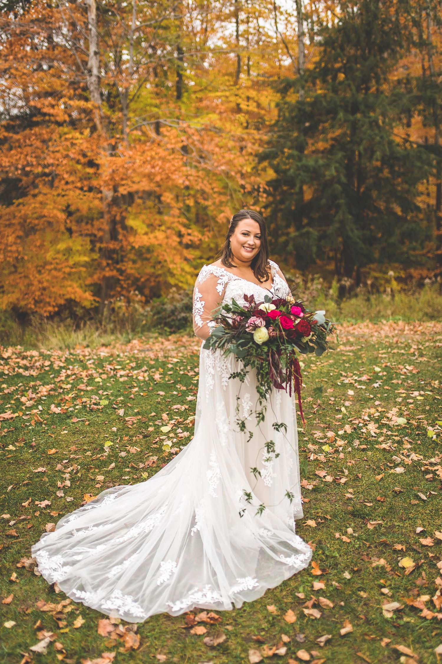 White wedding dress spreads beautifully across fallen autumn leaves in a forest setting.