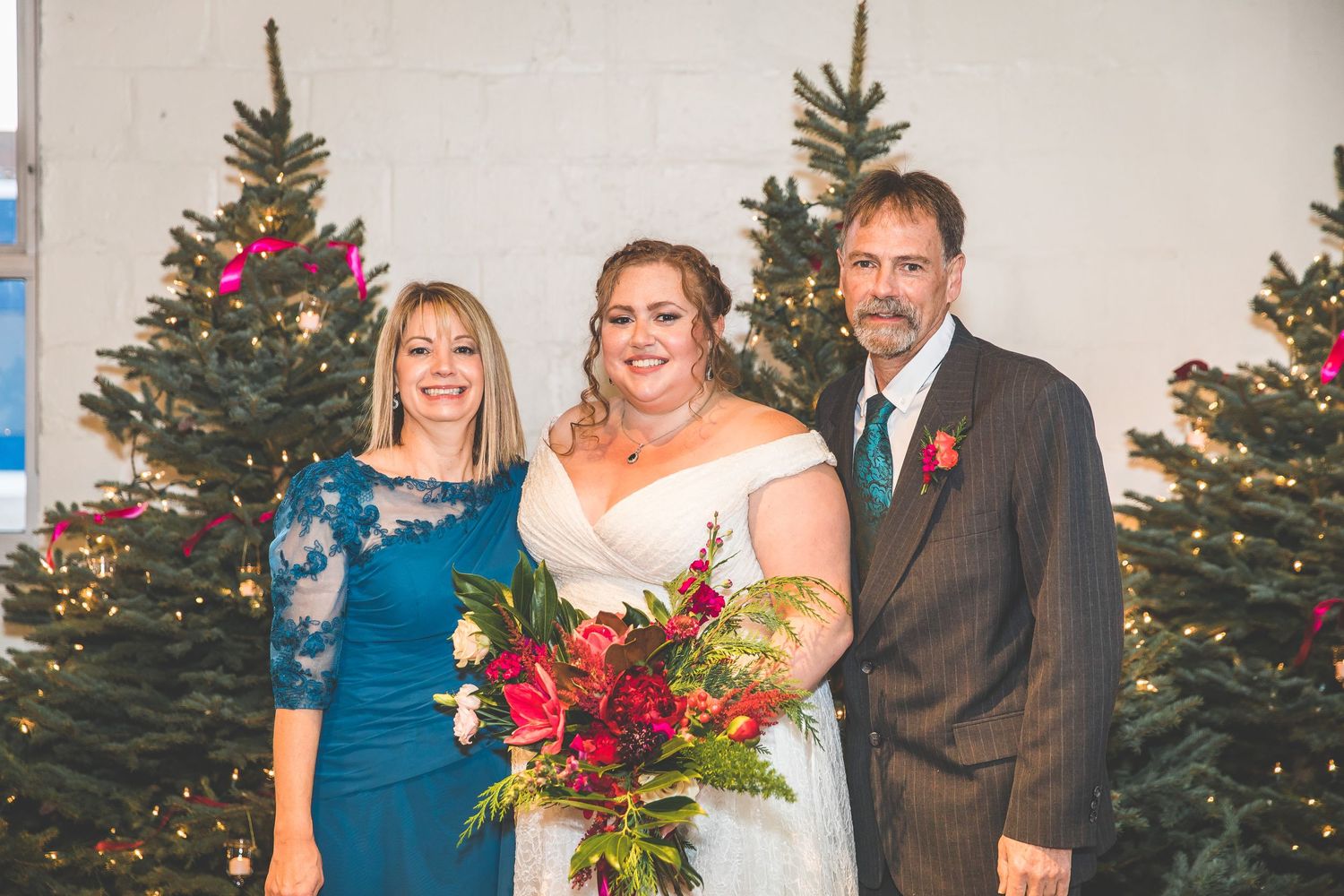 Wedding party poses in front of decorated Christmas trees with red floral arrangements.