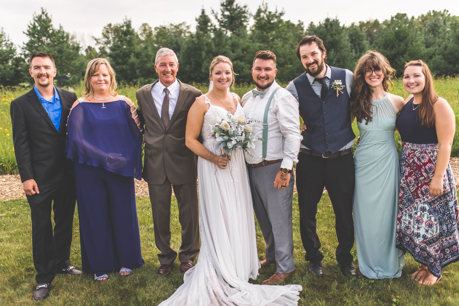 Wedding party members in light blue and gray attire pose together outdoors.