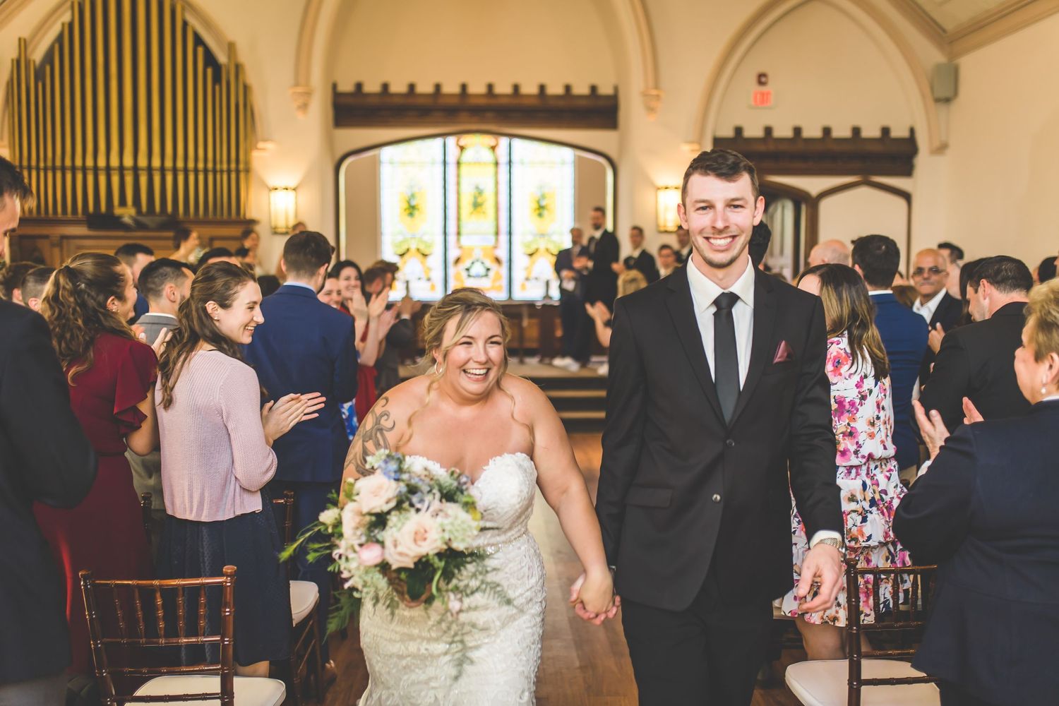 Wedding celebration in a grand church hall with guests applauding the happy couple.