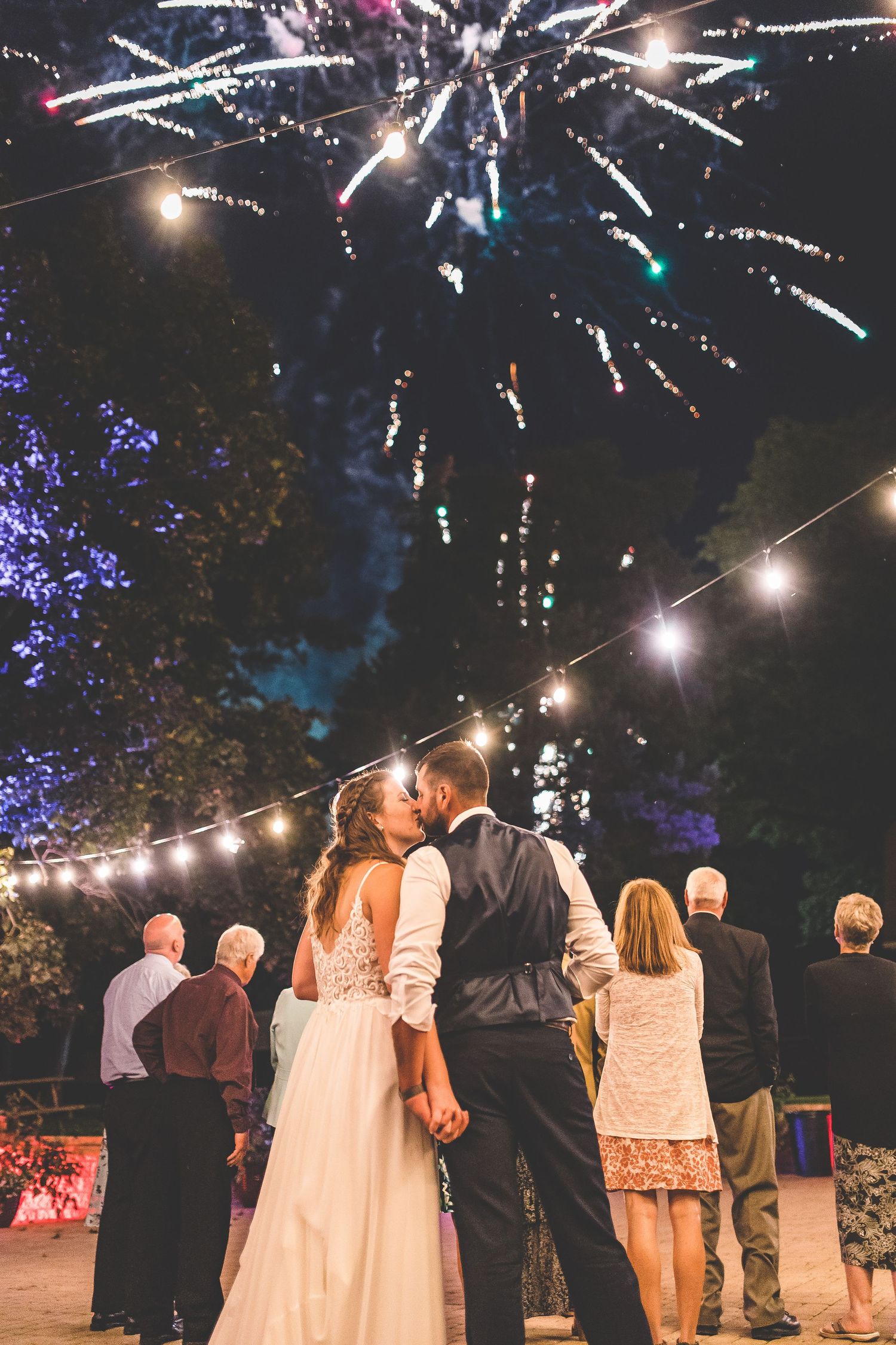 Wedding guests watch fireworks display during outdoor nighttime celebration.