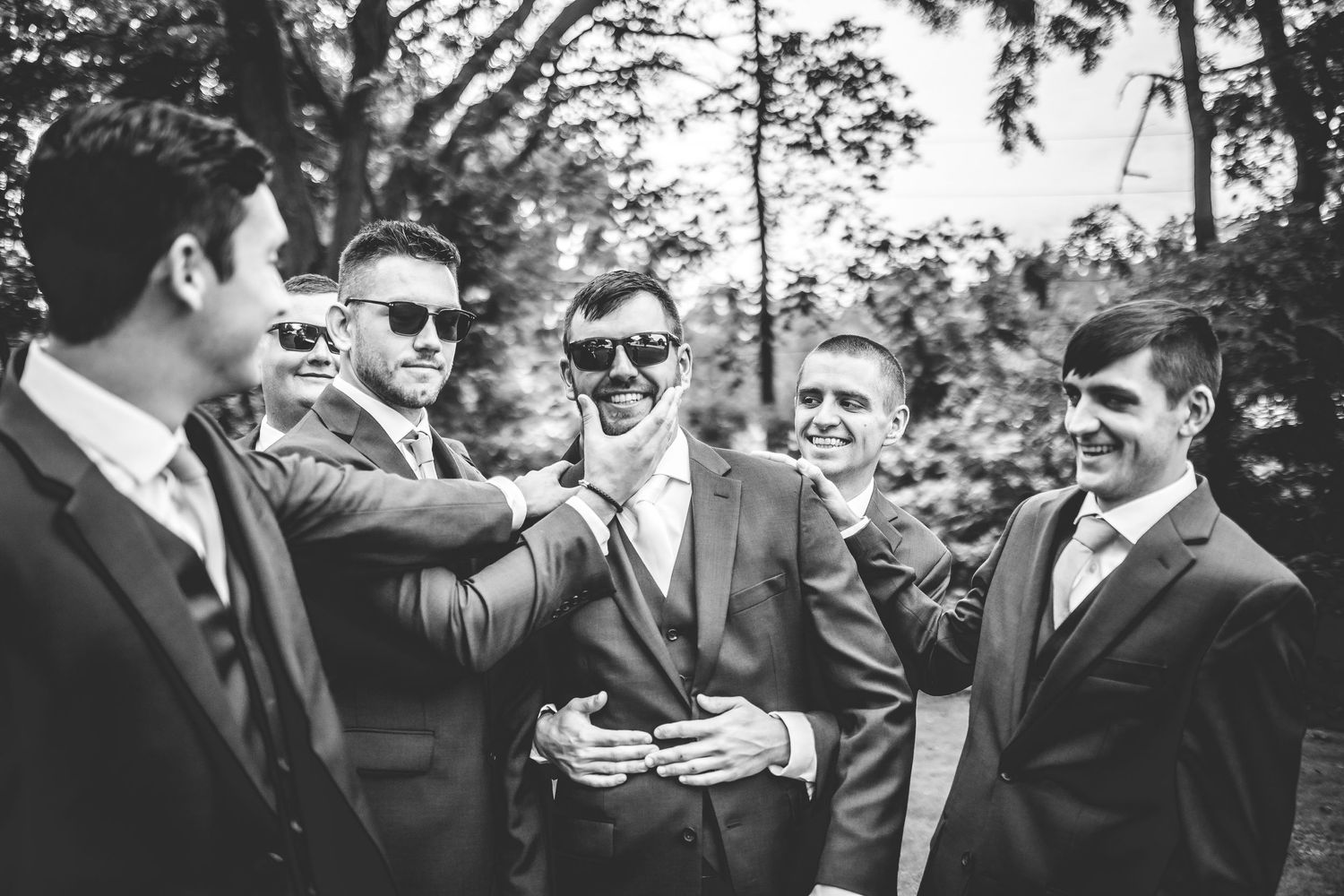 Black and white photo of groomsmen laughing together outdoors.