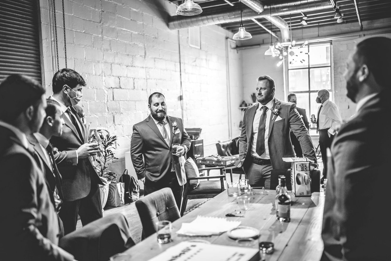 Black and white photo of groomsmen getting ready in an industrial-style room with brick walls.