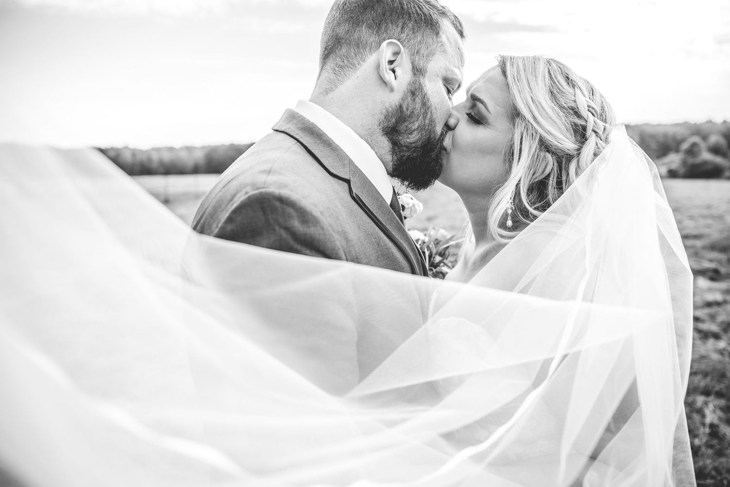 Intimate wedding moment captured through delicate white veil in natural outdoor setting.