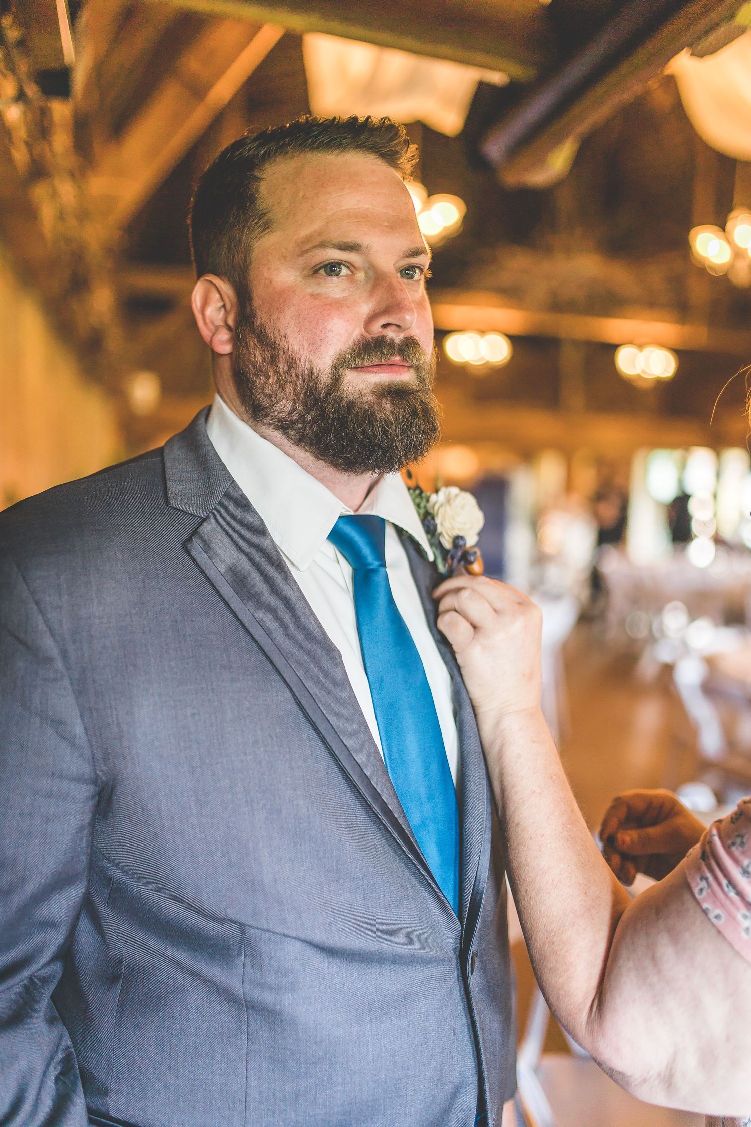 Groom in grey suit and bright blue tie during an emotional moment at rustic barn wedding venue.