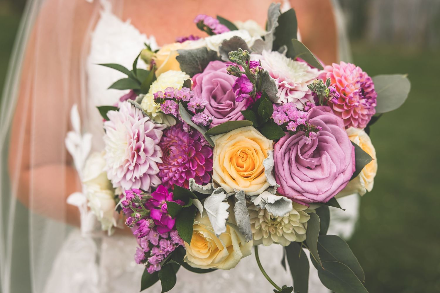 Elegant wedding bouquet featuring purple and peach roses with mixed greenery and florals.
