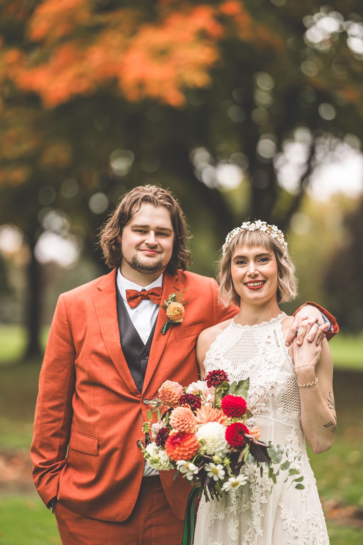 A couple in wedding attire poses with bright autumn foliage creating a stunning natural backdrop.