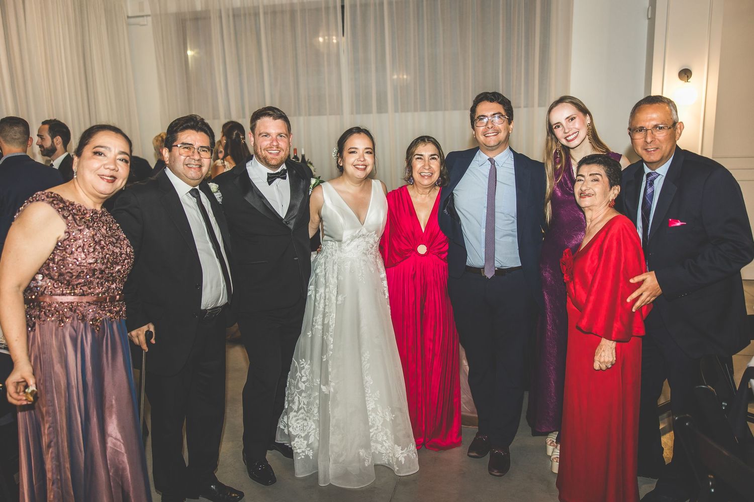 Wedding party and guests pose together in formal attire at an elegant indoor venue.