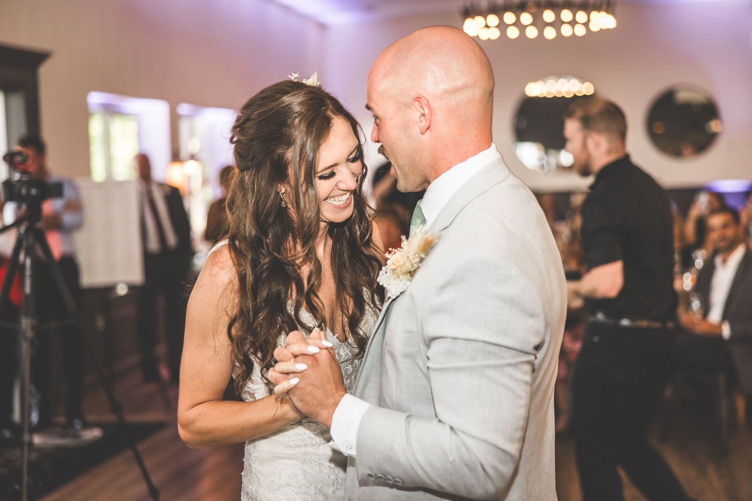 Couples slow dancing at a wedding reception under warm chandelier lighting.