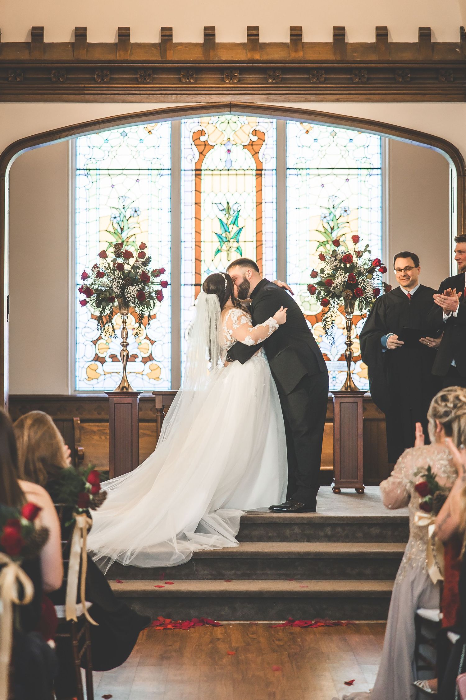 Church wedding ceremony with wooden pews and decorative stained glass windows in the background.