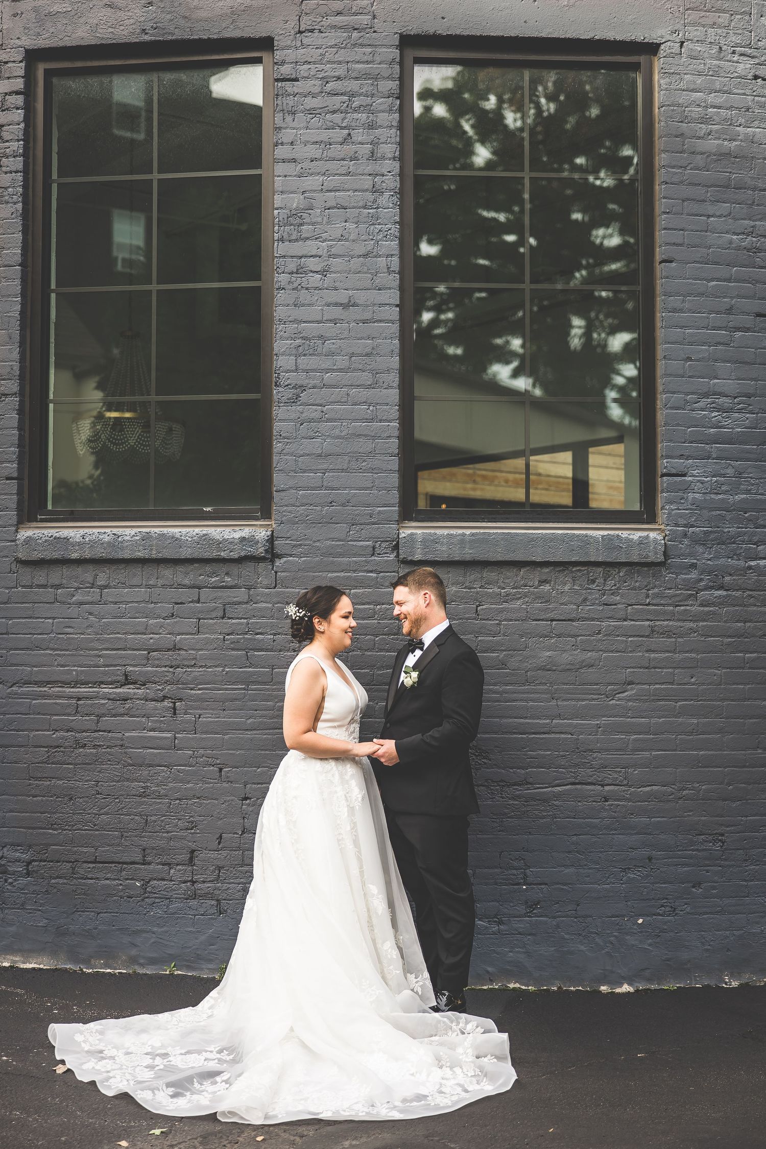 Wedding couple sharing an intimate moment against a dark painted brick wall exterior.