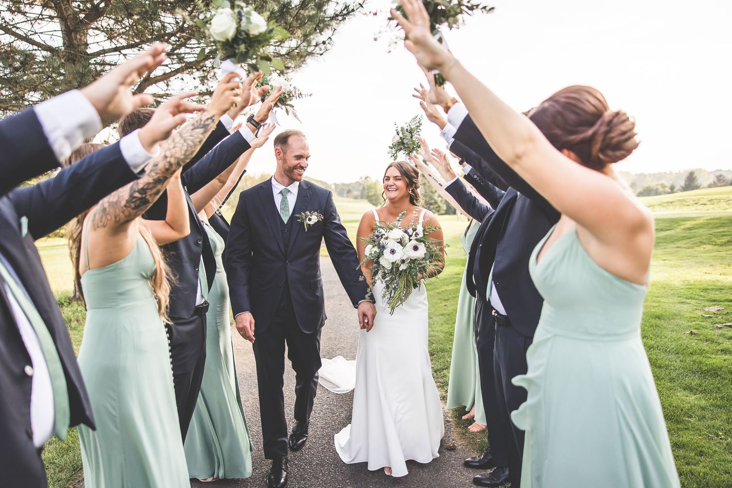 Wedding party forms celebratory arch tunnel for couple to walk through.