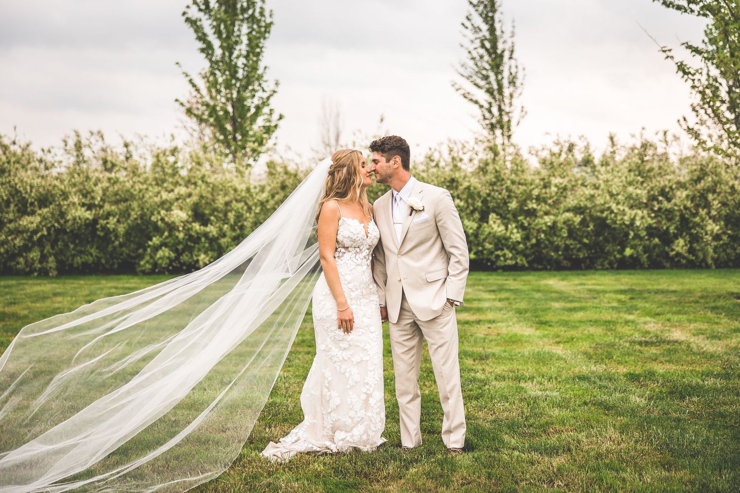 Romantic outdoor wedding portraits in a green field with flowing veil and natural lighting.