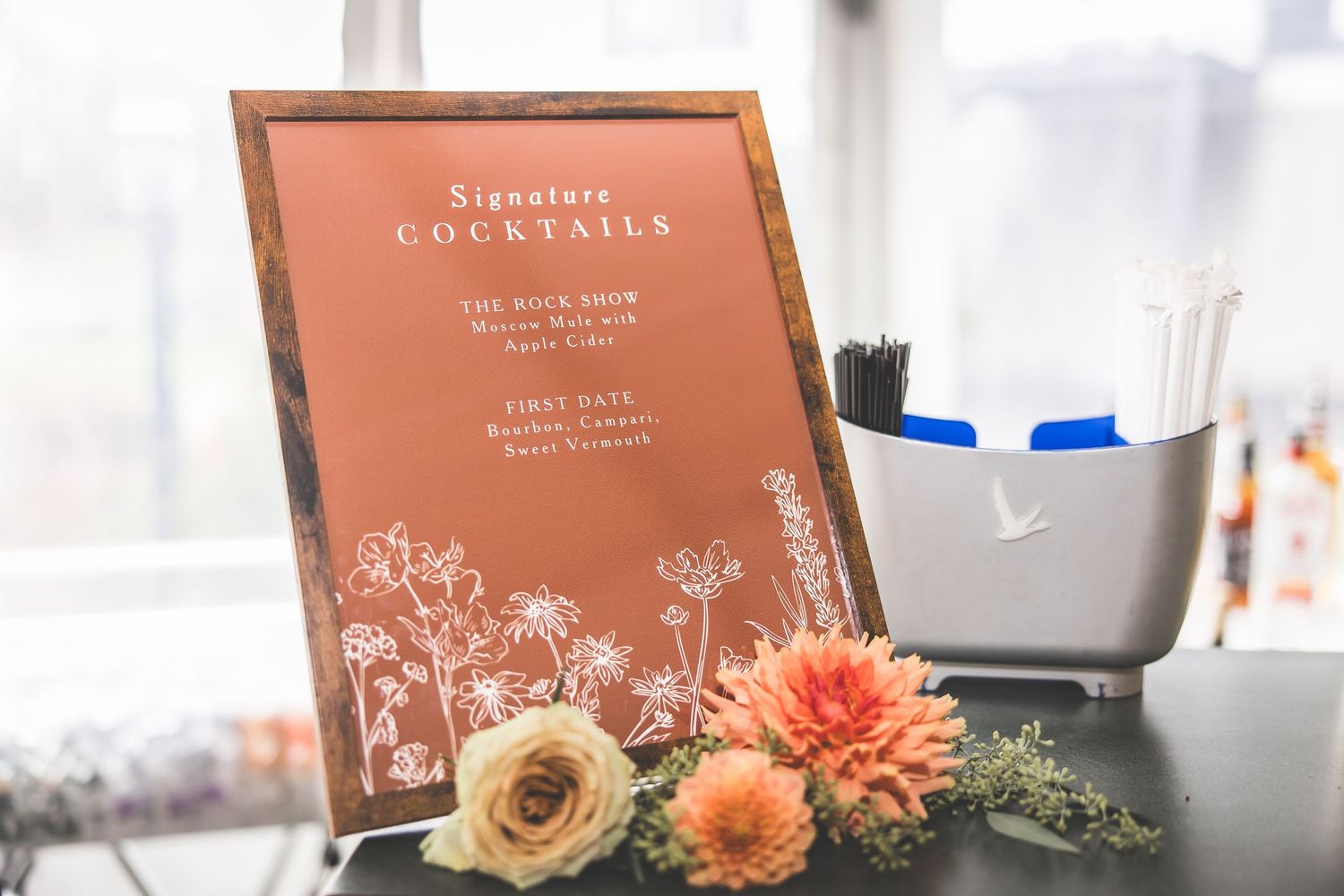 Wedding cocktail menu with floral design displayed alongside peach and cream flowers.