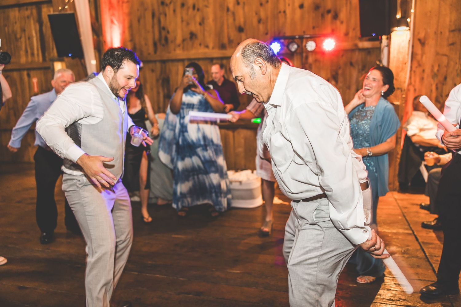 Wedding party members dancing and celebrating on a wooden dance floor under ambient lighting.
