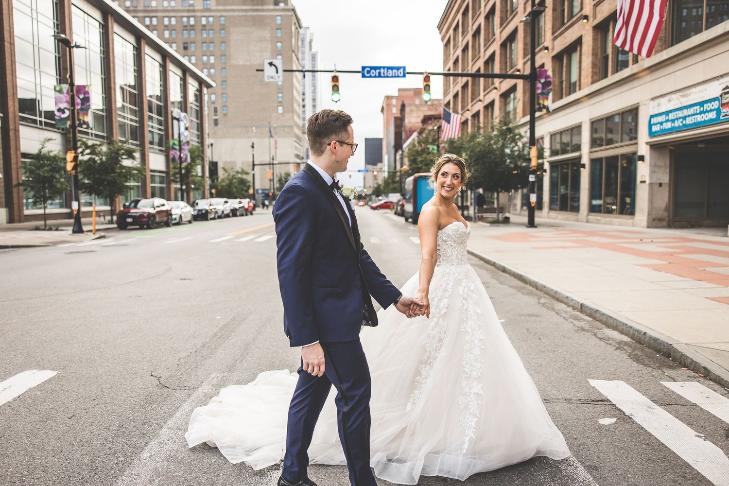 Bride and groom share joyful dance moves on empty downtown street with American flag visible.