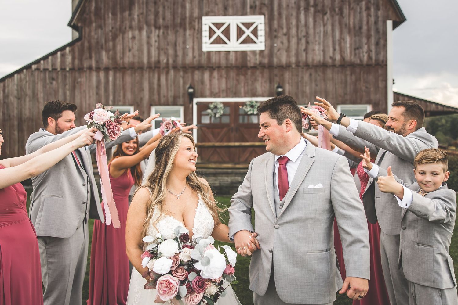 Wedding party gathers for group photos in front of wooden barn with classic white trim.