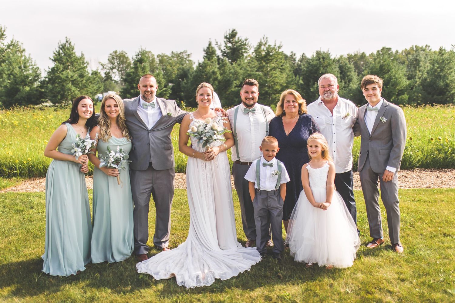 Wedding party poses together in an outdoor field with trees and natural scenery in the background.