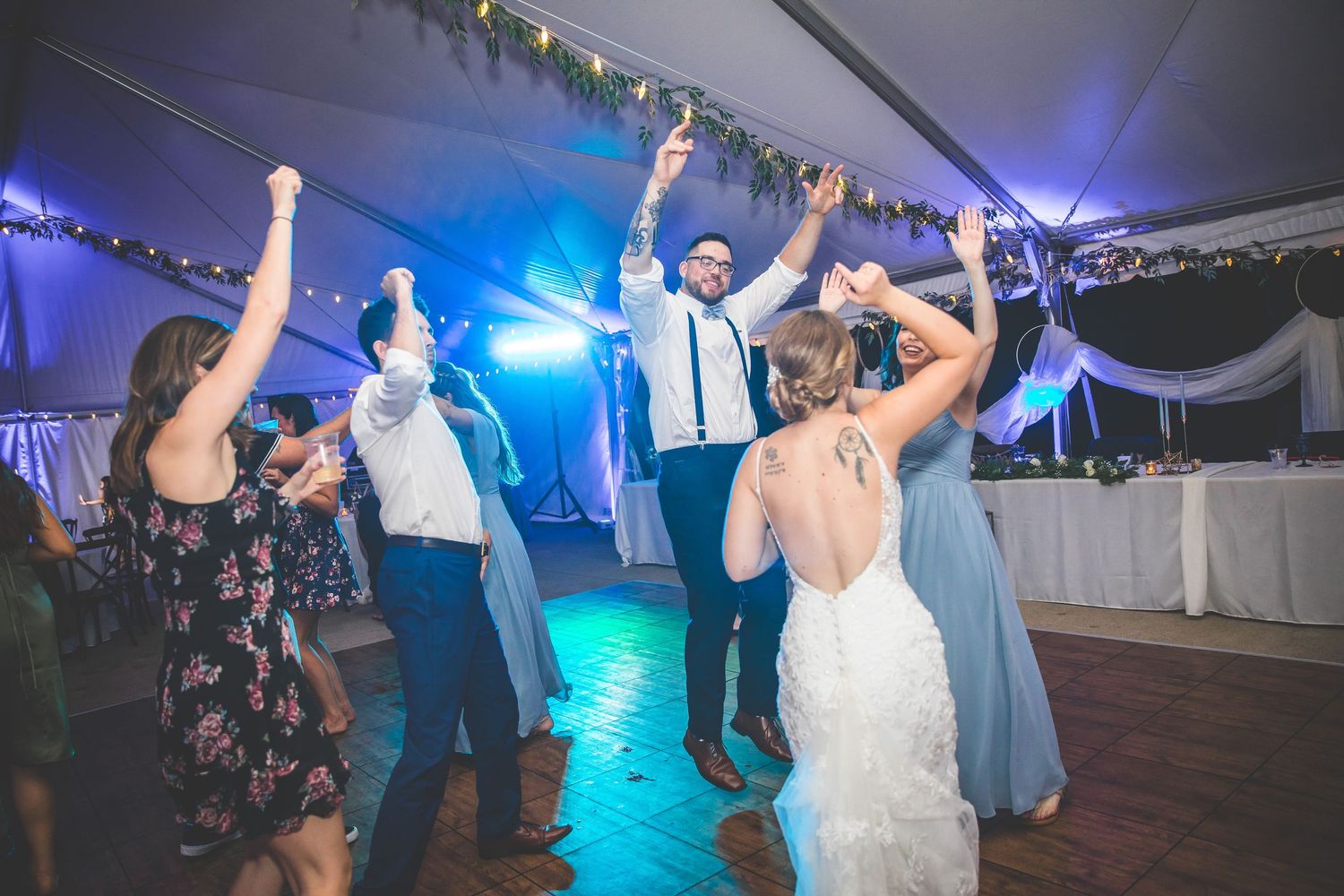 Wedding reception dance party with colorful blue lighting and guests dancing in a white tent venue.