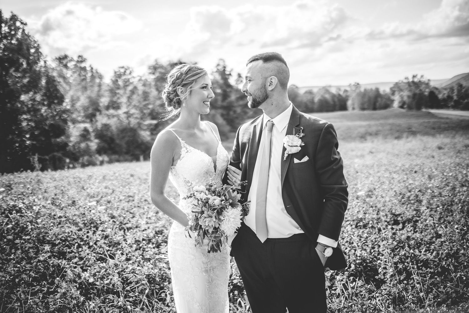 A couple shares a romantic moment in a sunlit field with rolling hills in the background.