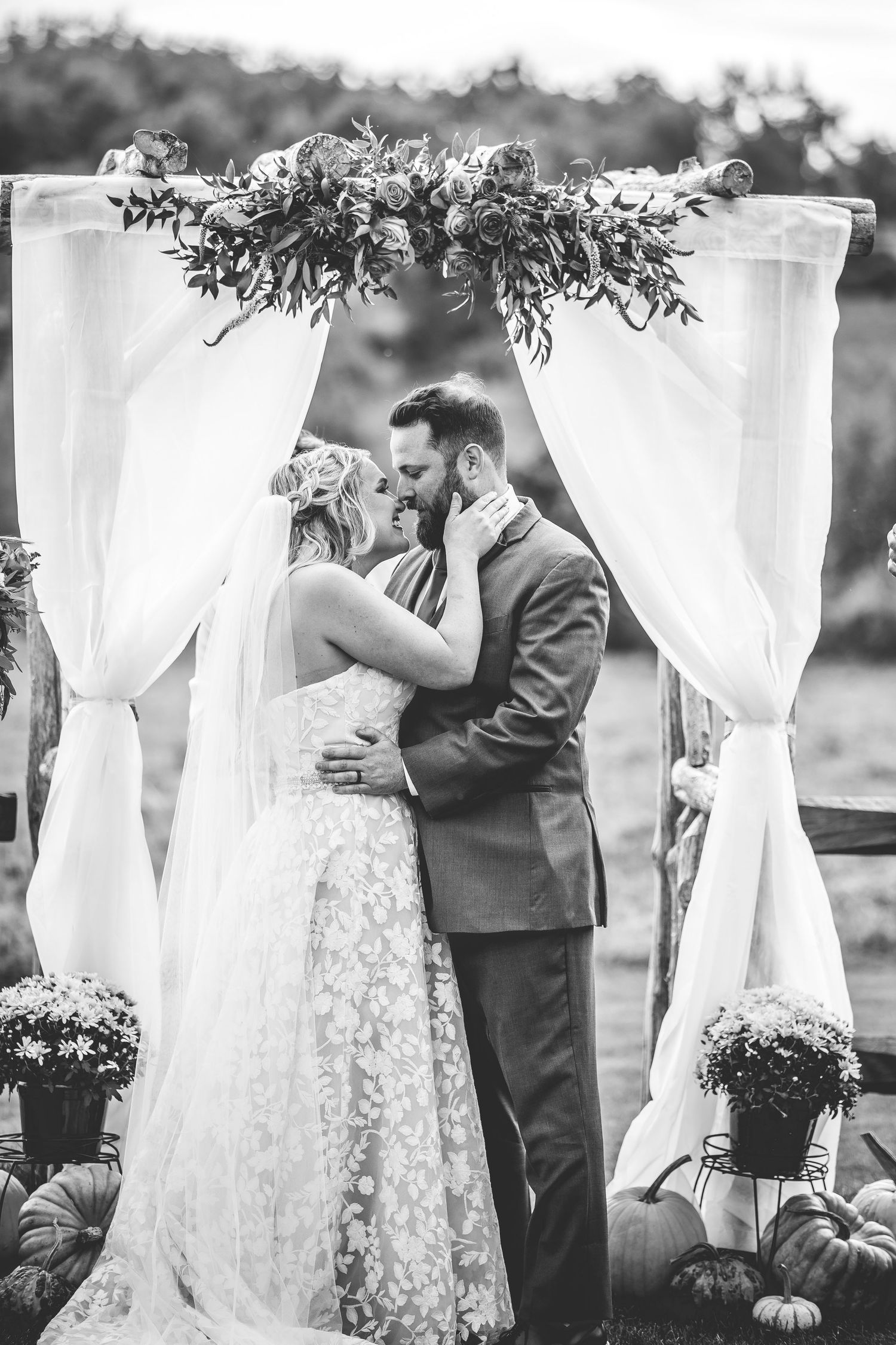 Wedding ceremony under white draped arch with floral decorations in outdoor garden setting.