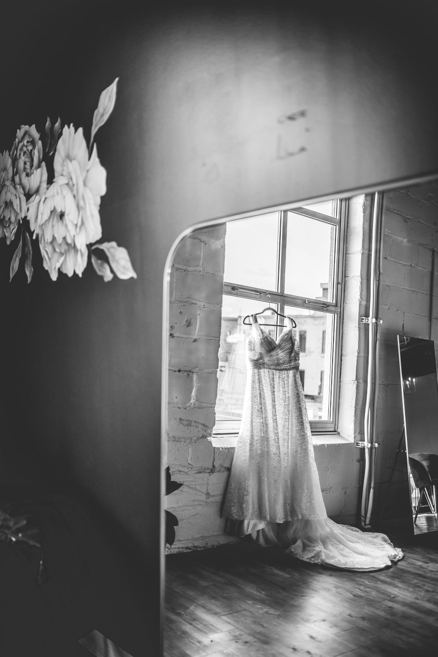 Elegant white wedding dress hanging in window light creating dramatic shadows in empty room.