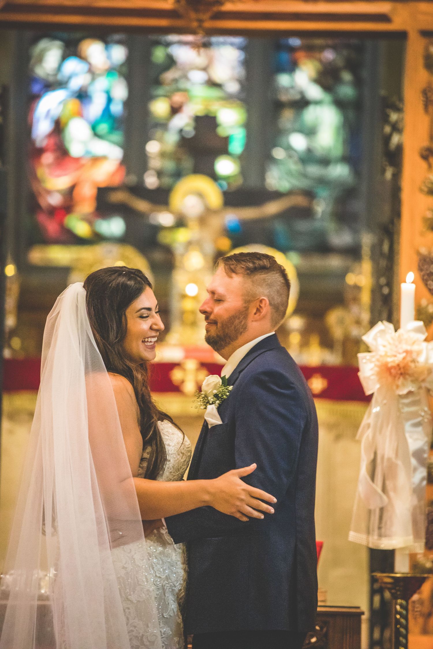 A romantic moment captured during a wedding ceremony in a church with warm lighting and stained glass windows.