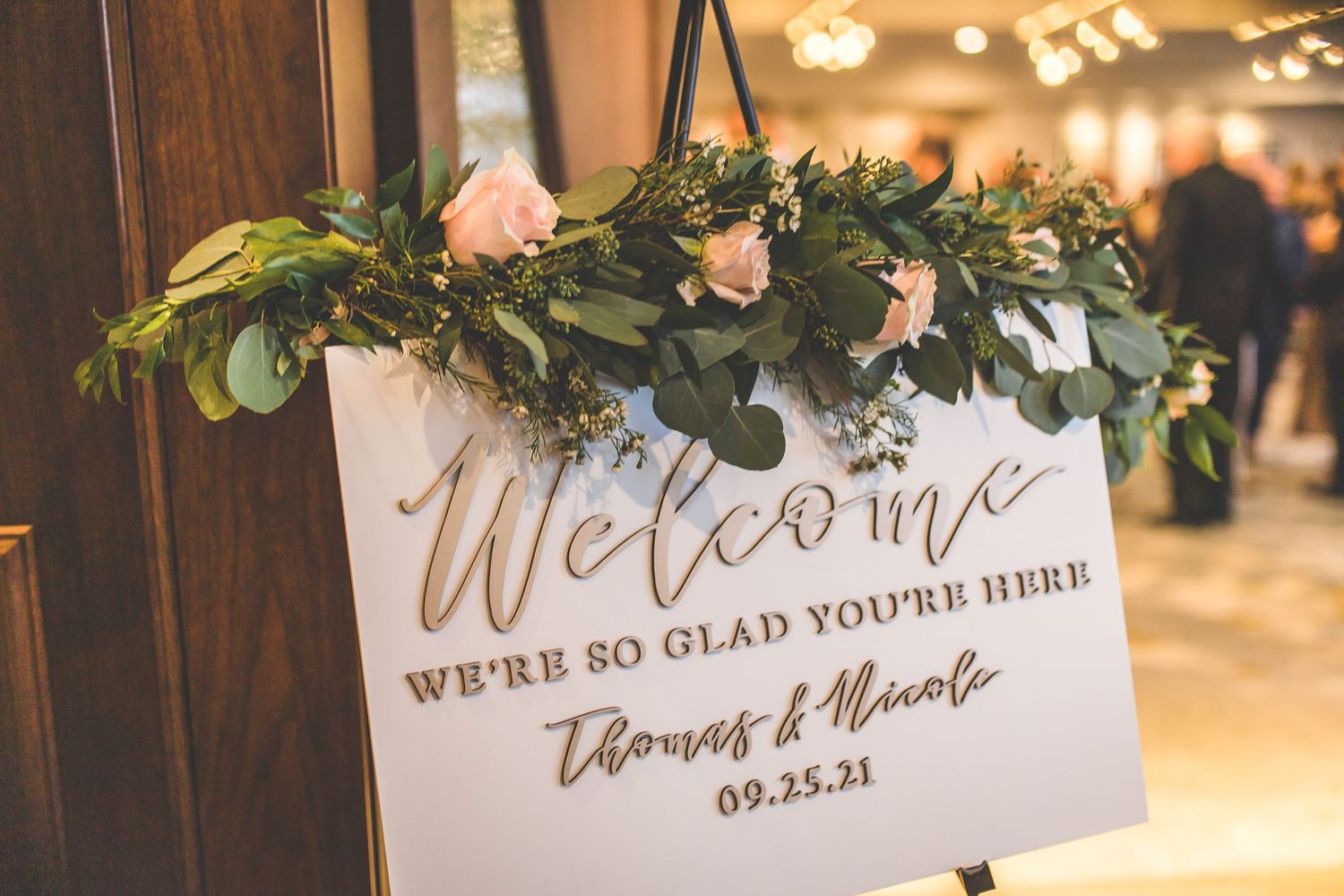 Wedding welcome sign decorated with greenery and blush pink floral arrangements.