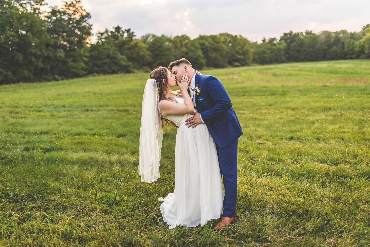 A couple sharing a romantic kiss in a green meadow during golden hour.