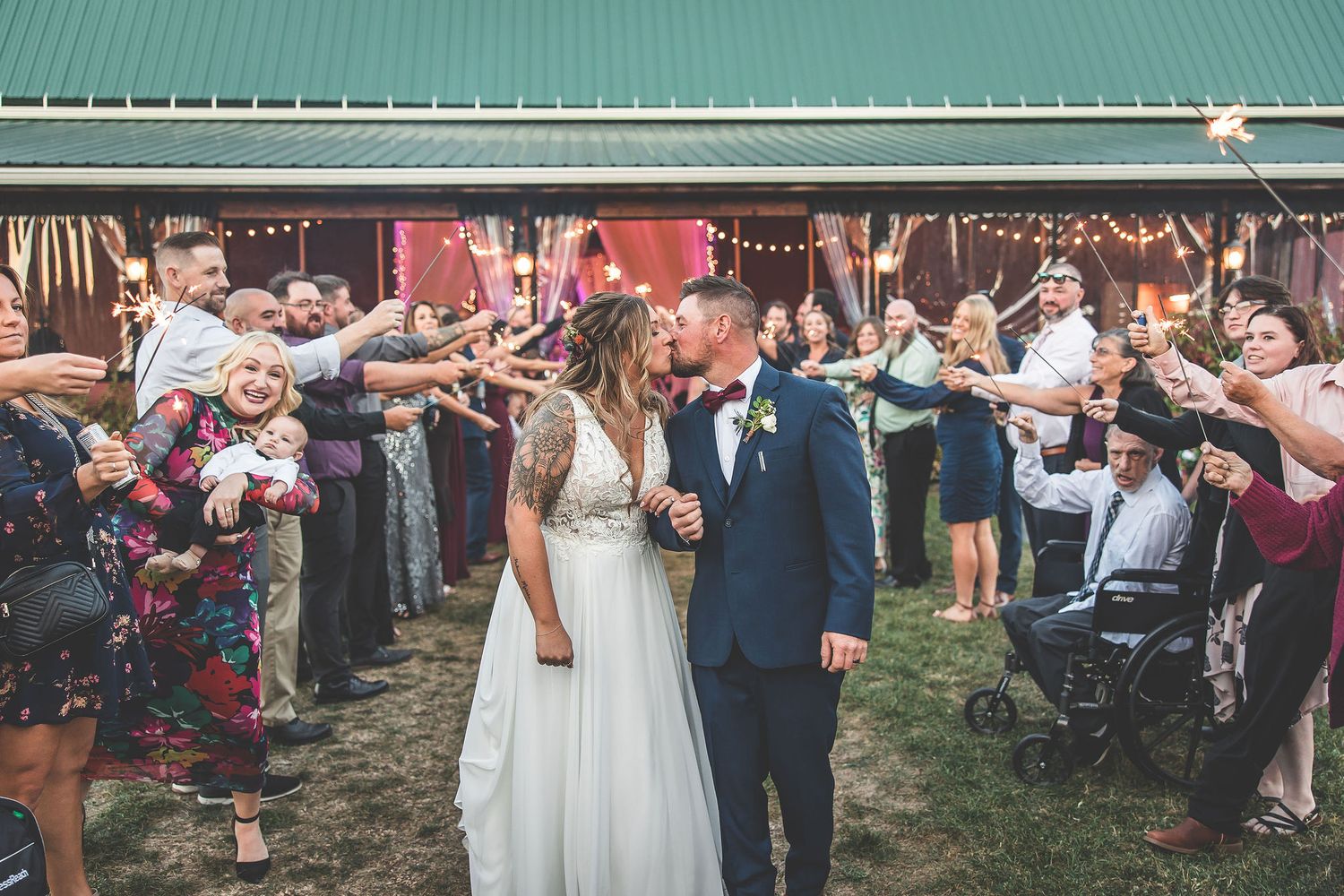 Wedding couple walks through sparkler exit line outside barn venue.