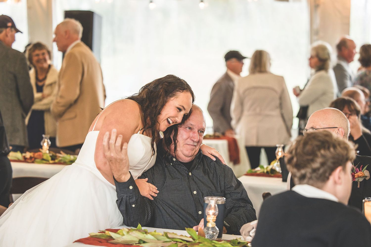 Reception guests enjoying conversations and celebrations under white tent lighting.