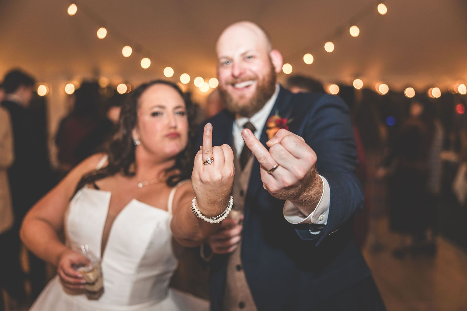 Wedding guests dancing and celebrating under warm string lights at an evening reception.