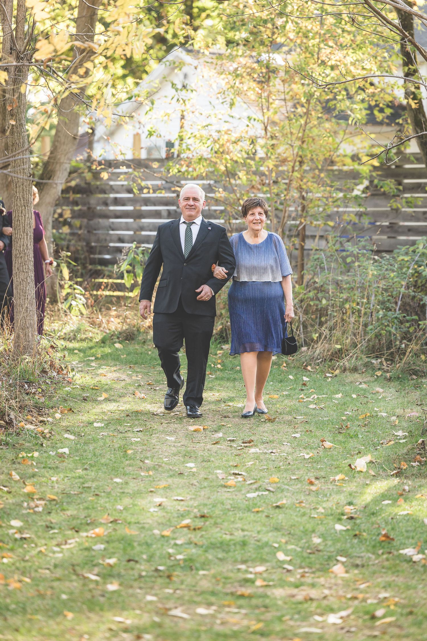 Wedding processional walking through an autumn garden path with natural lighting.