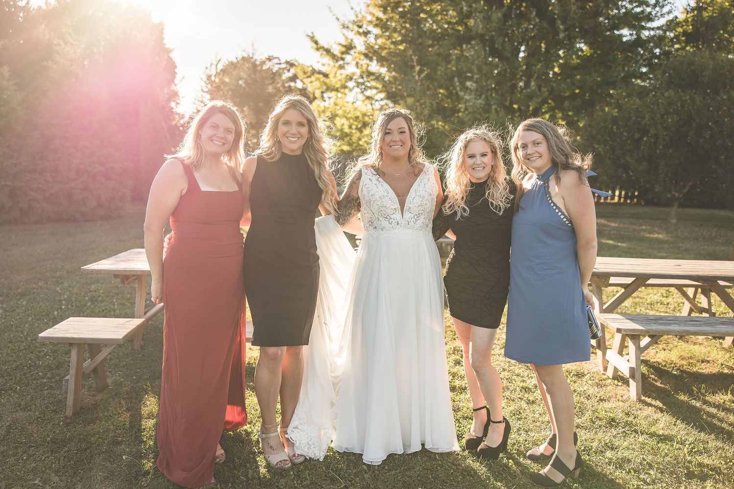 Wedding party gathers for outdoor photos during golden hour by rustic venue.