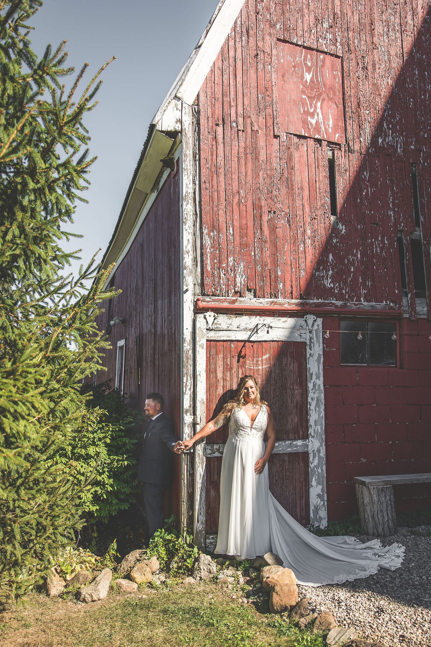 A classic red barn serves as a backdrop for a wedding photoshoot on a sunny day.