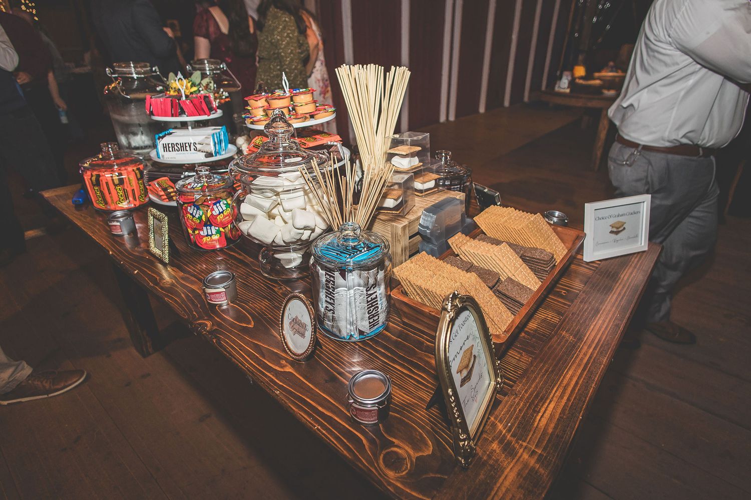 A rustic wooden table displays an assortment of desserts and treats at a wedding reception.