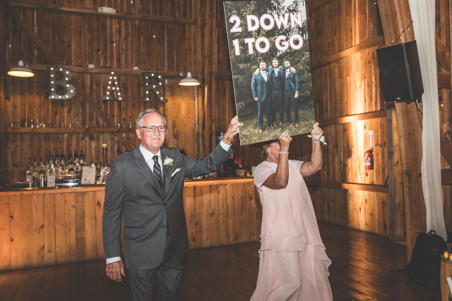 Wedding reception dance floor in rustic barn venue with decorative lighting and signage.