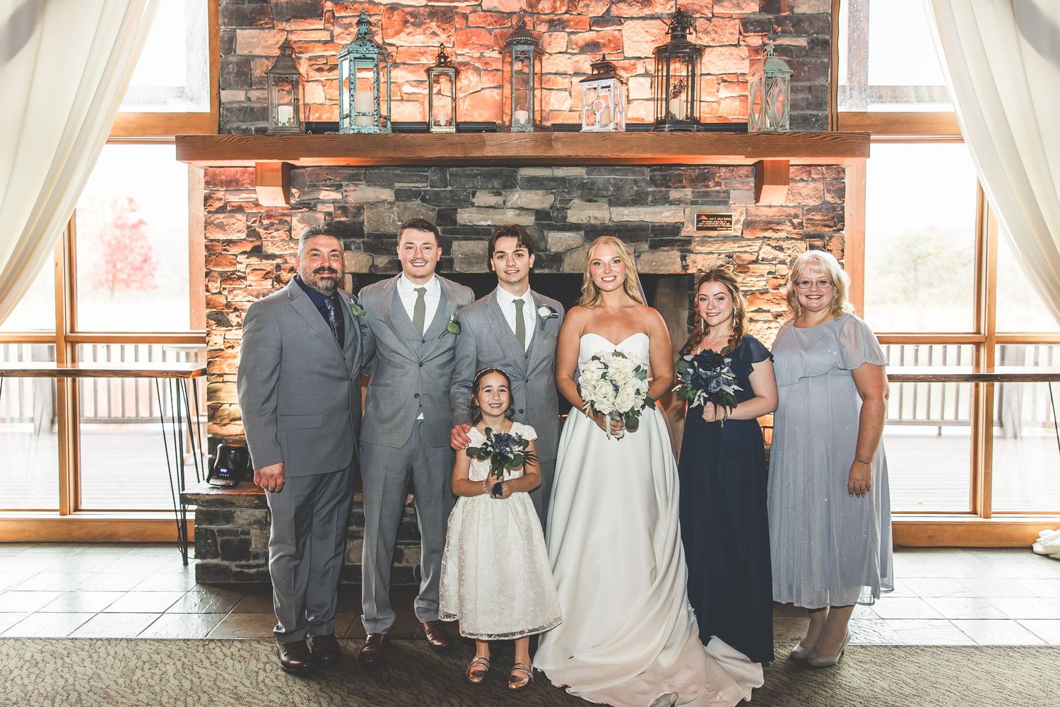 Wedding party poses in front of rustic stone fireplace at elegant venue.