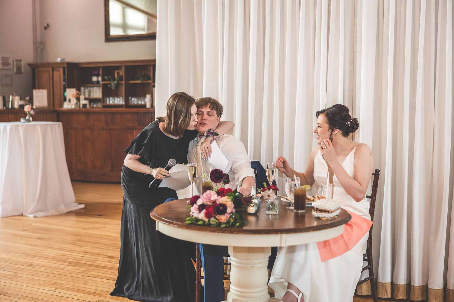 Wedding celebration in progress at an elegant venue with white drapes and round tables.