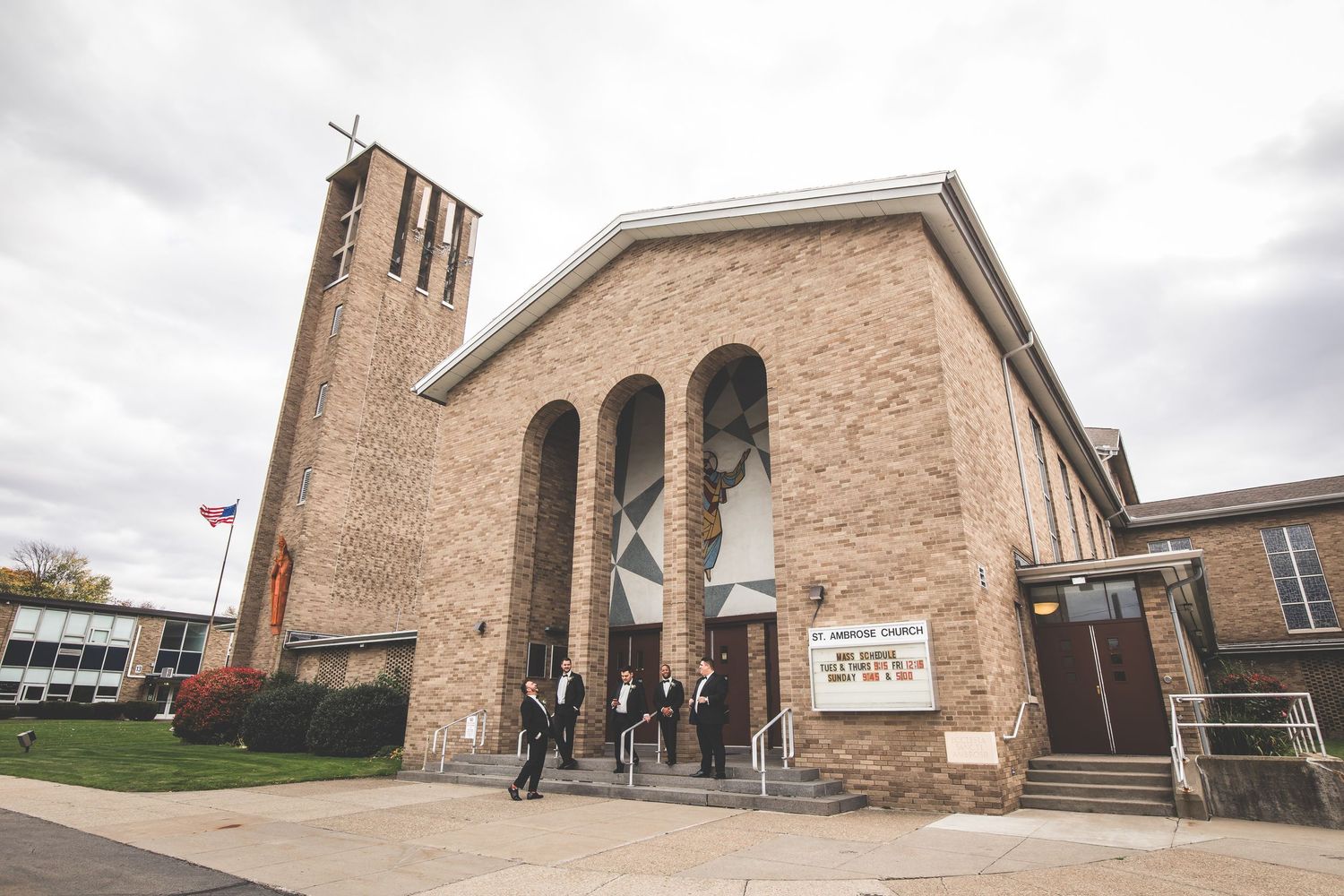 Modern brick church building with tall bell tower and arched windows under cloudy sky.