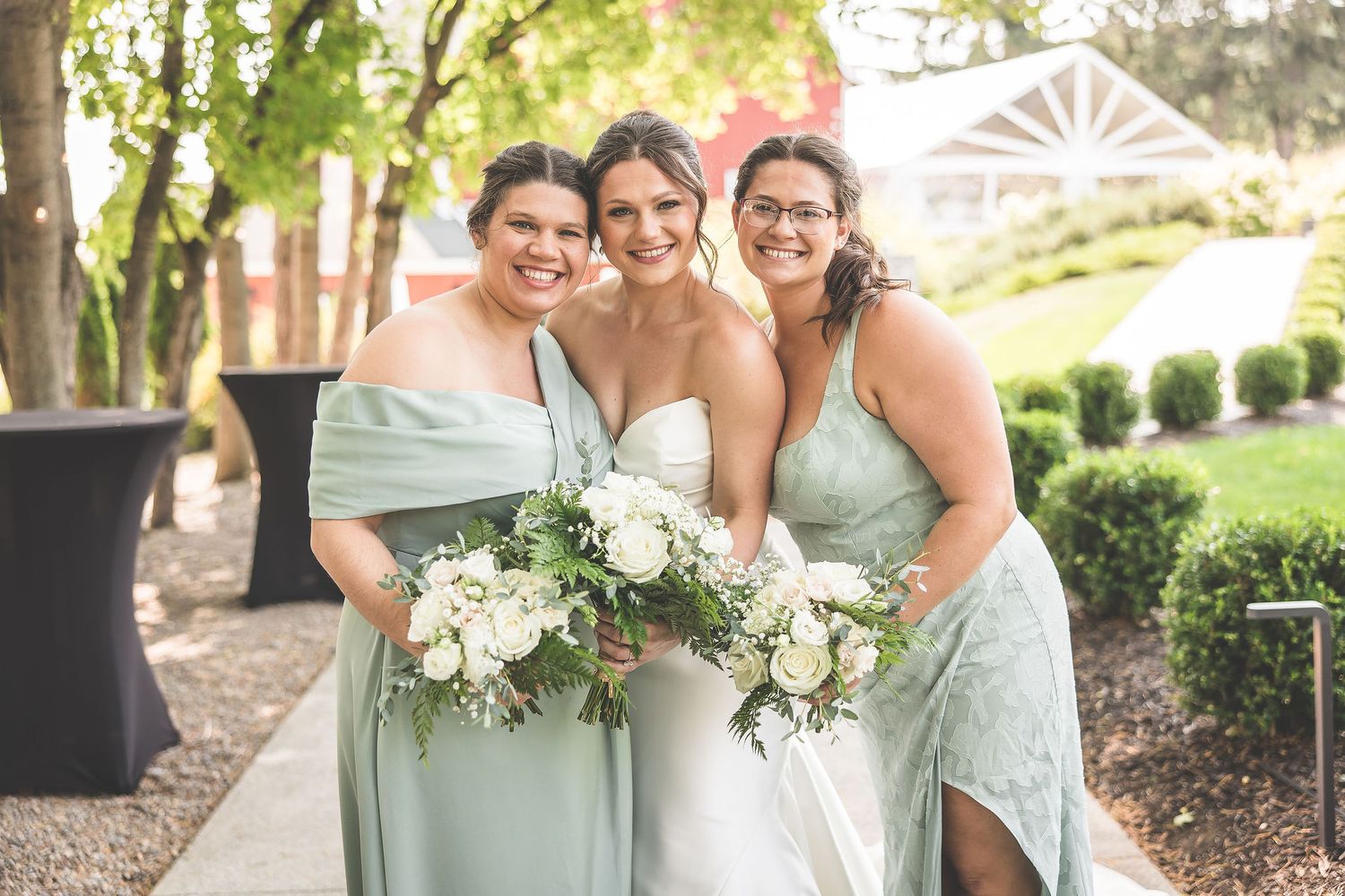 Wedding party members share joyful moments together in a garden setting wearing sage and white attire.
