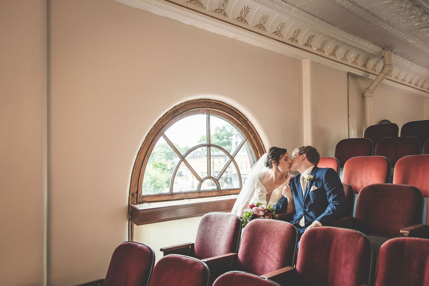 Elegant theater setting with arched windows and vintage details frames a wedding moment.