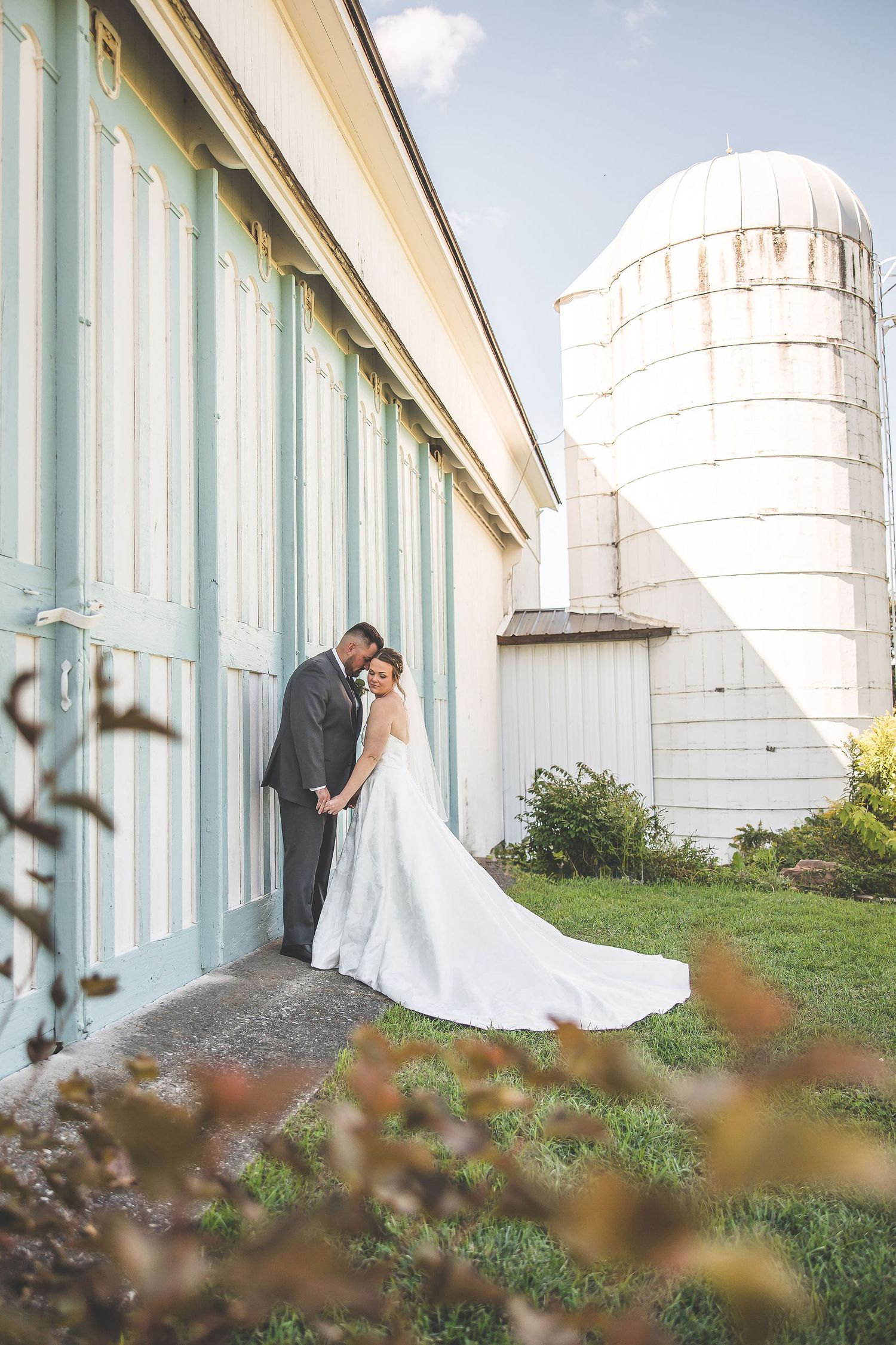 Wedding portraits against a white farm building with distinctive silos creating a rustic backdrop.