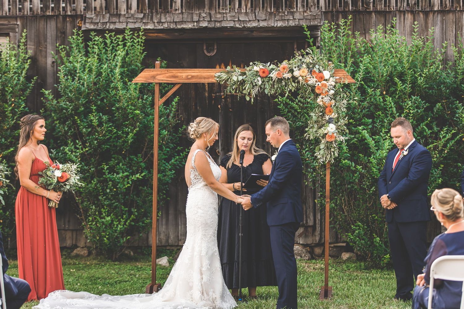 Rustic outdoor wedding ceremony with wooden backdrop and floral decorations.